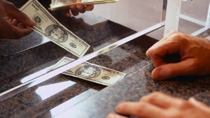 Person, Human, Money Remittance flow between the kingdom of Saudi Arabia and Kenya rose 30.28% in the first eight months of 2023 bank teller handing over dollars at a counter cash