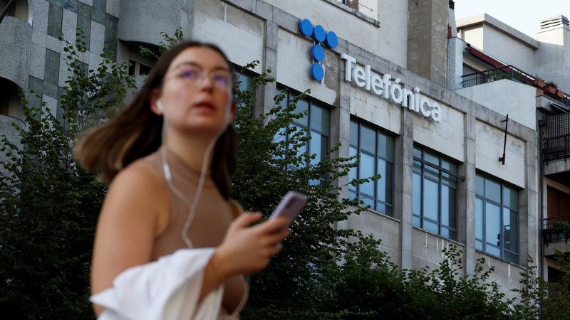 A woman walks past a building displaying the logo of Spanish telecom company Telefonica
