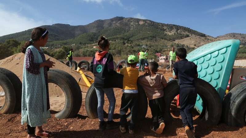 Children displaced by the earthquake look on as workers build a playground for them at the Regraga camp