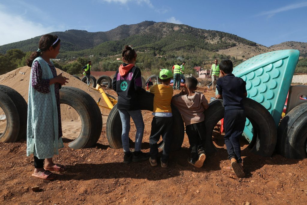 Children displaced by the earthquake look on as workers build a playground for them at the Regraga camp