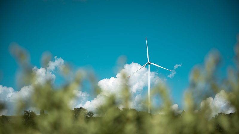 Wind turbine against blue sky with blurred green foreground greenwashing environment
