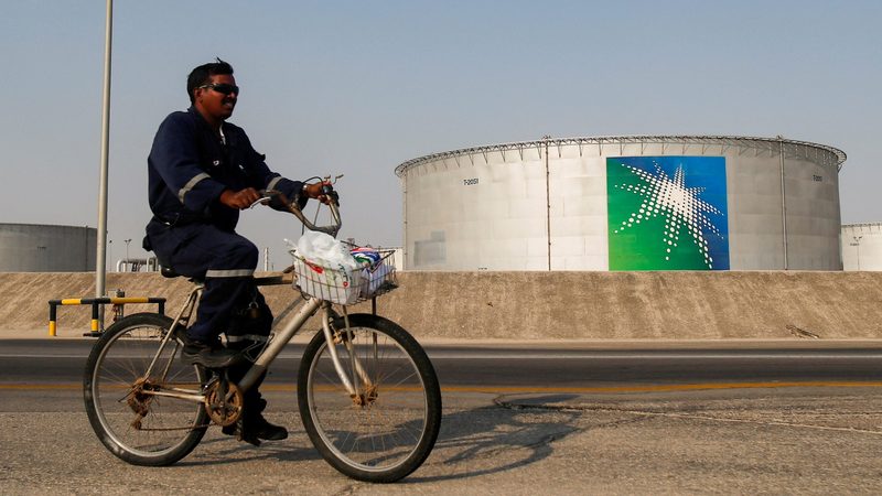 A worker cycles past Aramco oil tanks in Abqaiq, Saudi Arabia