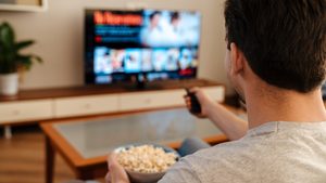 Man watching tv and eating popcorn at home on a couch, back view