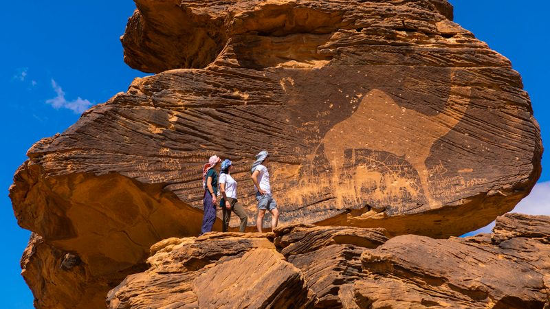 Tourists in front of the Jabal Al-Mawaqi rock art in Saudi Arabia