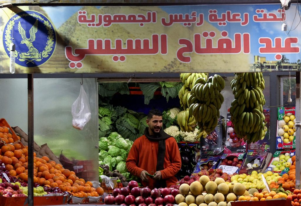 A market worker in Cairo stands under a pro-President Sisi banner. The ADQ deal has raised hopes that Egypt's economy can rebuild
