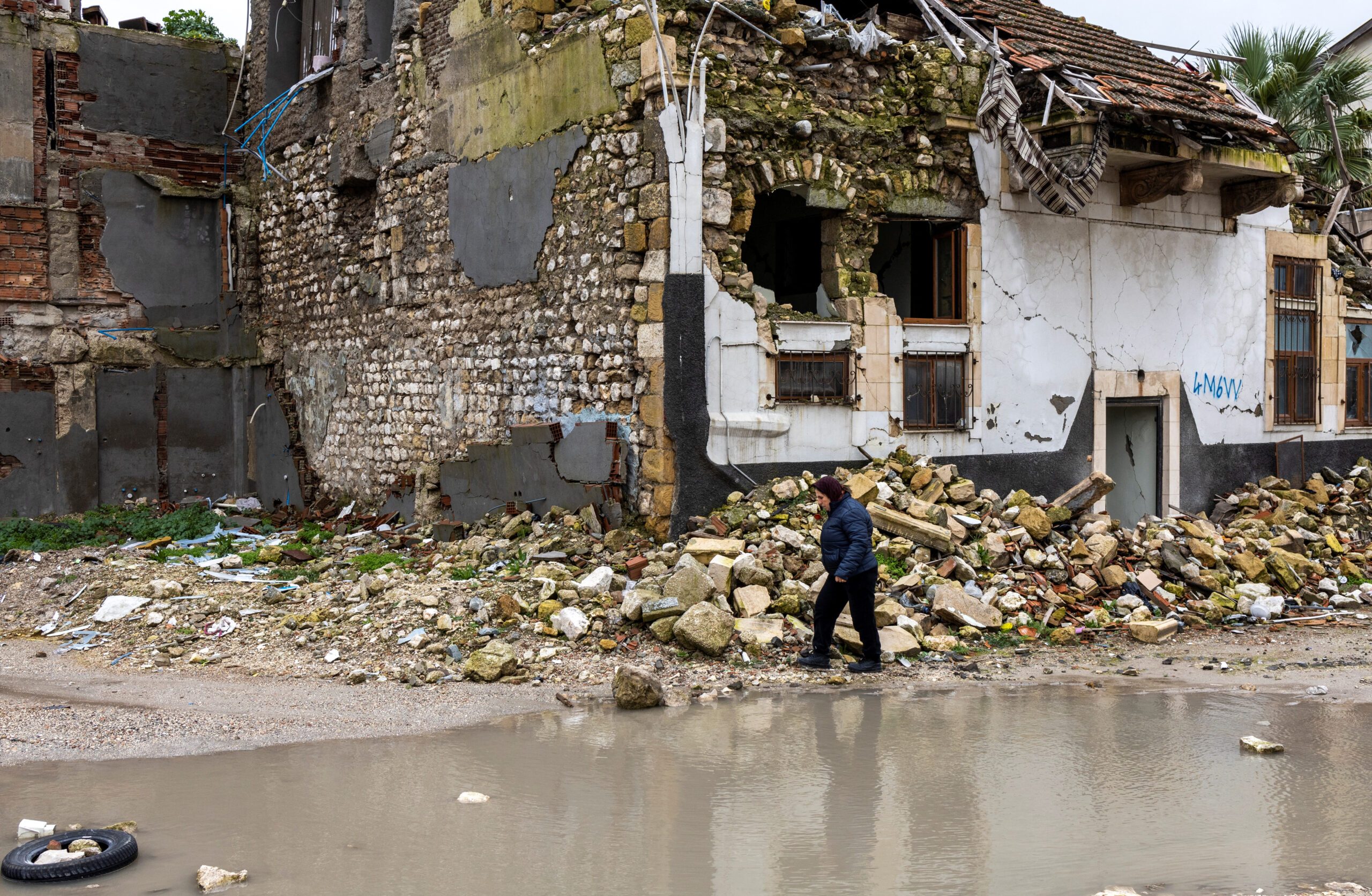 quake Turkey economy A woman walks past houses destroyed by last year's earthquake, in Hatay, Turkey,