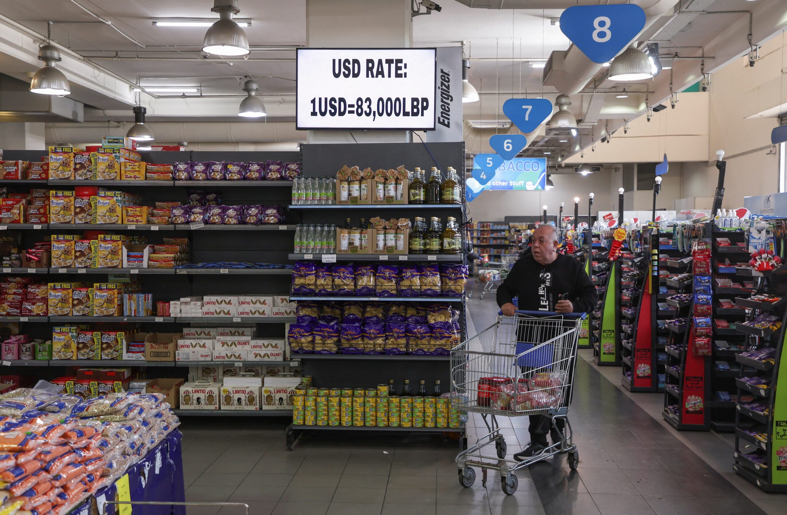 A man pushes a shopping cart near a screen showing the exchange rate of Lebanese pound to U.S. dollars inside a supermarket in Beirut, Lebanon March 9, 2023. REUTERS/Mohamed Azakir