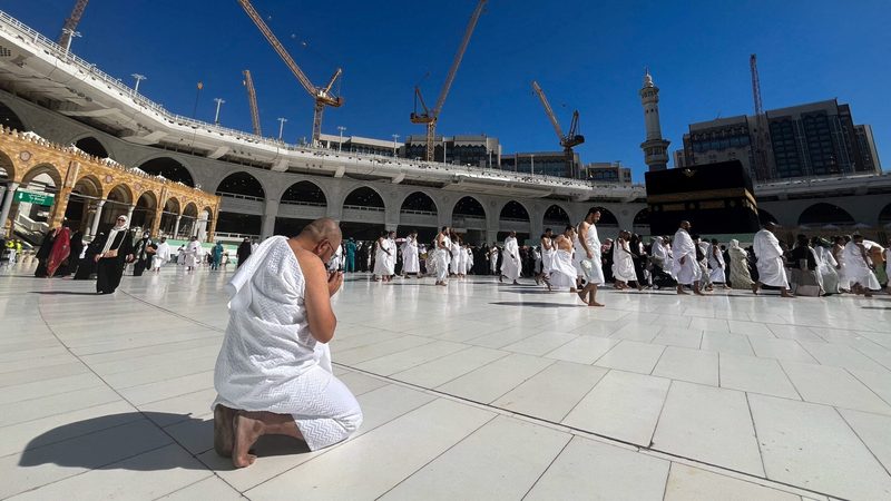 Construction cranes tower over the Grand Mosque in Mecca, as a pilgrim kneels in prayer