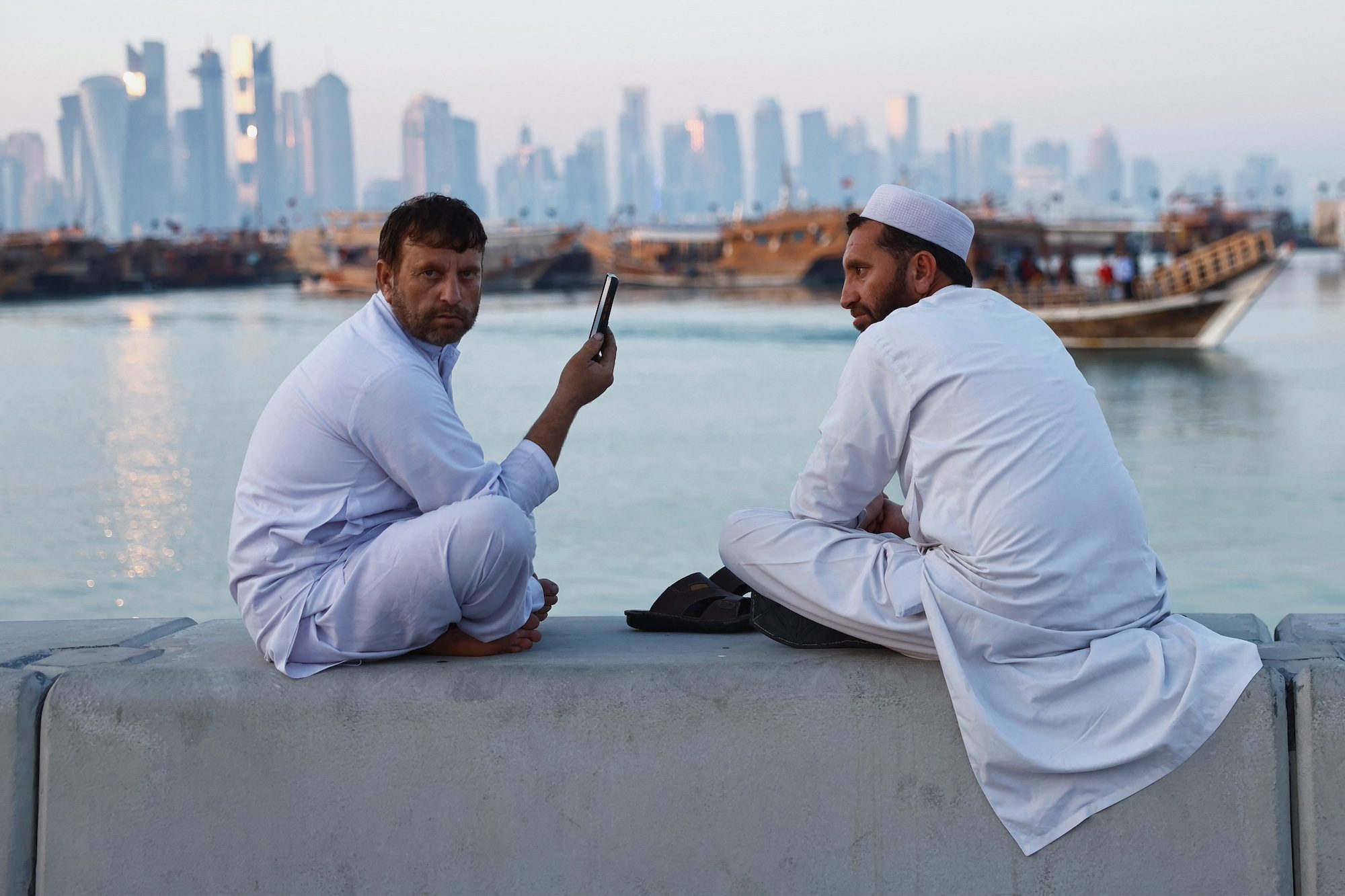 People rest on a wall at the Doha Corniche with the Doha skyline seen in the background in Doha, Qatar, February 13, 2024. REUTERS/Clodagh Kilcoyne