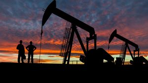 H50RFT Silhouette of oil workers at an oil field pumpjack site against a dramatic sky.