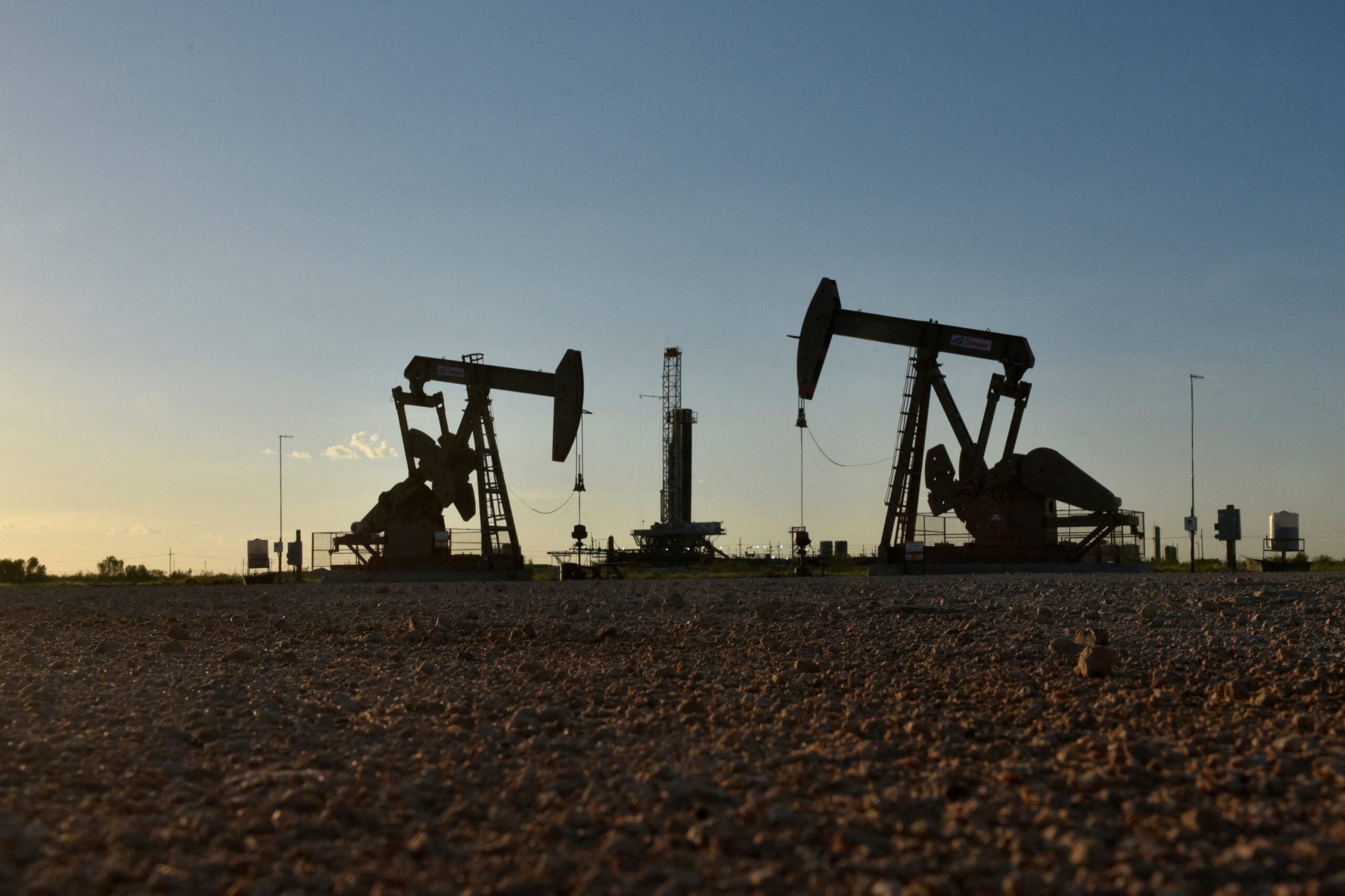 Pump jacks operate in front of a drilling rig in an oil field in Midland, Texas