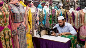 2A2Y7P1 A tailor in his shop sitting in front at a sewing machine with colorful dresses in Muscat, Oman