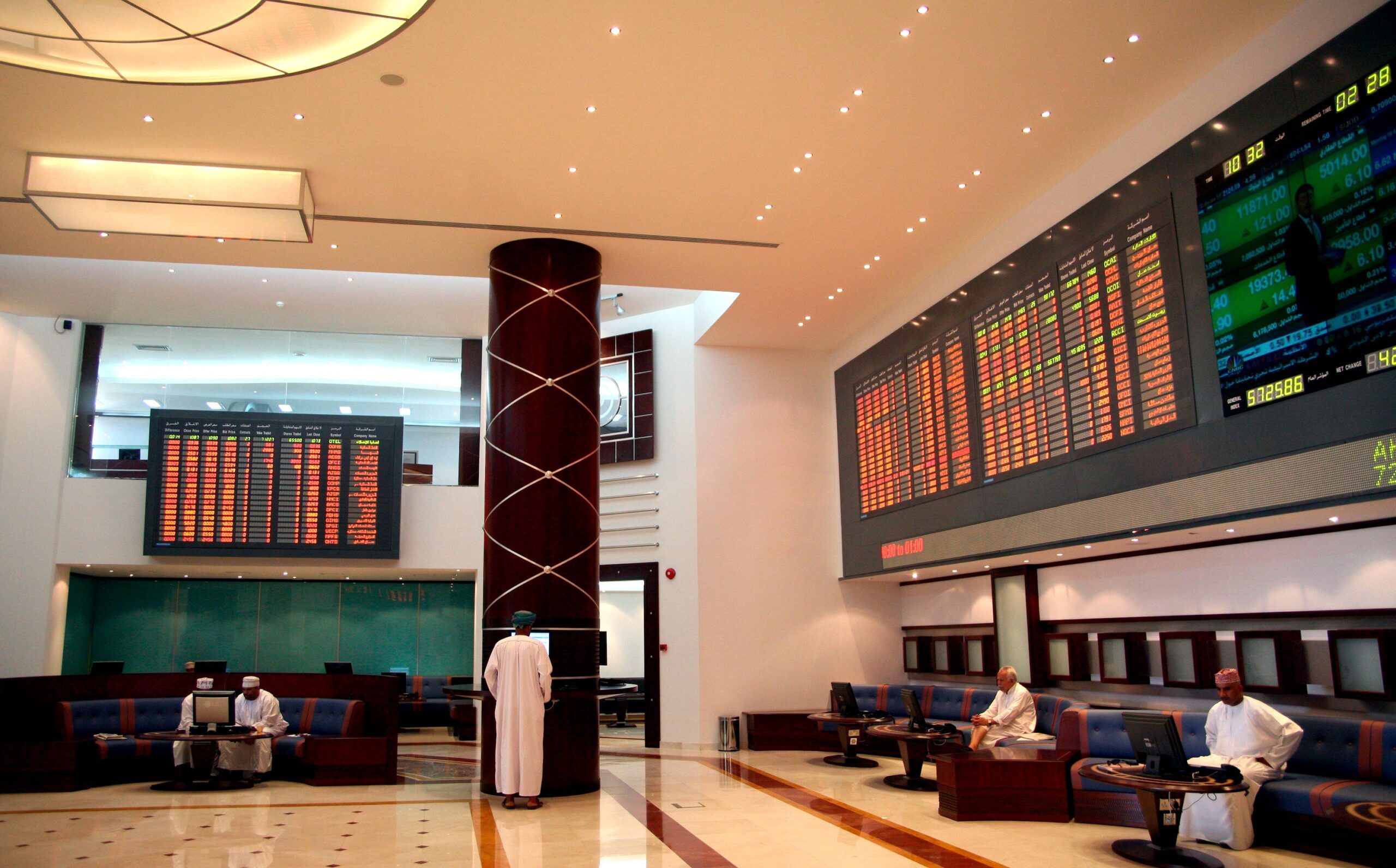 Investors check prices at Oman's stock exchange. OQ Base Industries is due to list in December