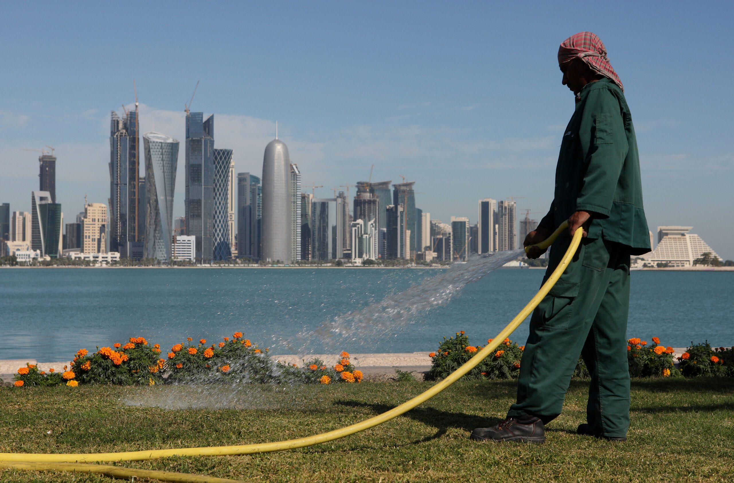 Gardener watering plants on the Corniche with West Bay skyline of Doha in the background.