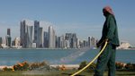 Gardener watering plants on the Corniche with West Bay skyline of Doha in the background.
