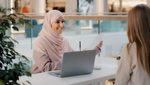 2J862E6 Young arab woman consultant sales agent bank worker sitting at office desk advises unrecognizable girl client offers to sign contract sale agreement