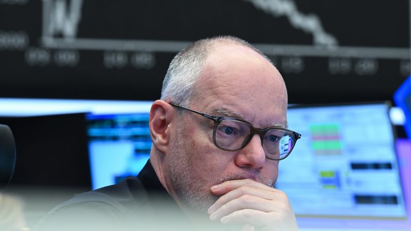 A stock market trader watches his monitors on the trading floor of the Frankfurt Stock Exchange while the display board with the Dax curve shows falling prices.