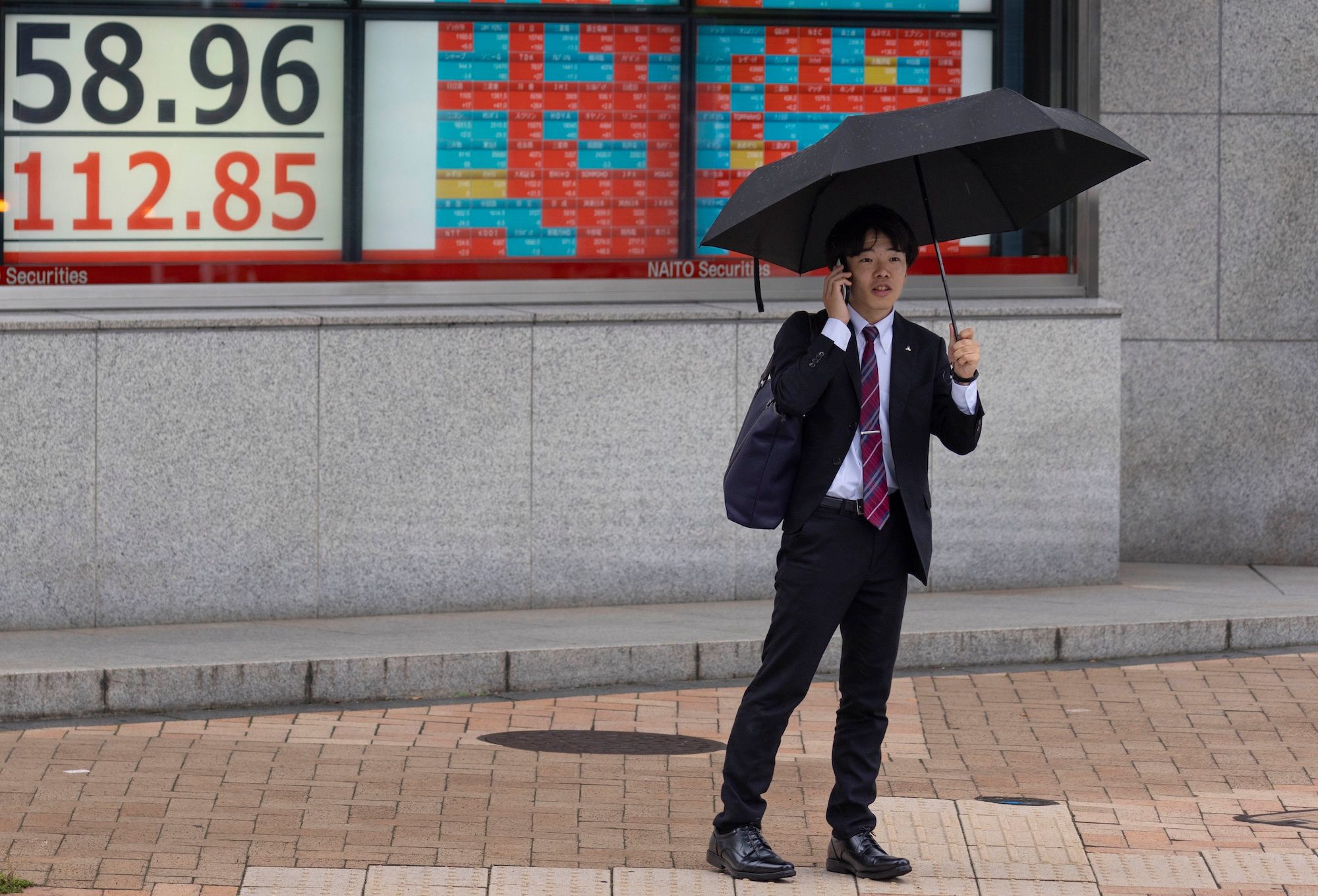 Businessman stands in front of a live view of the Nikkei index