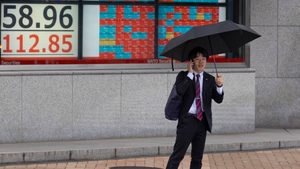 Businessman stands in front of a live view of the Nikkei index