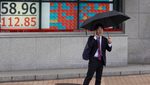 Businessman stands in front of a live view of the Nikkei index