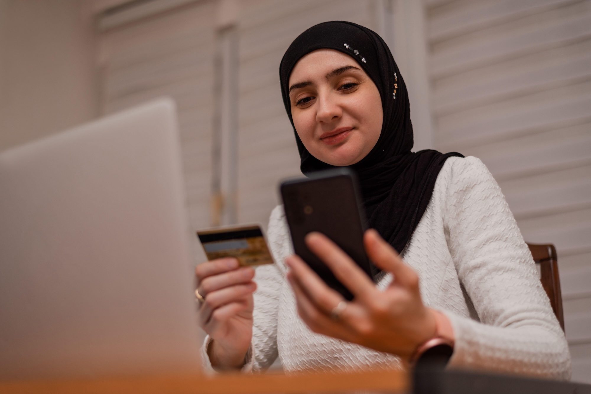 2YJHBFX A young happy Muslim woman using mobile phone and holding credit card checking balance account or making money transfer. Online Payment Internet