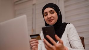 2YJHBFX A young happy Muslim woman using mobile phone and holding credit card checking balance account or making money transfer. Online Payment Internet