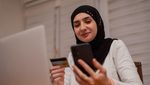 2YJHBFX A young happy Muslim woman using mobile phone and holding credit card checking balance account or making money transfer. Online Payment Internet