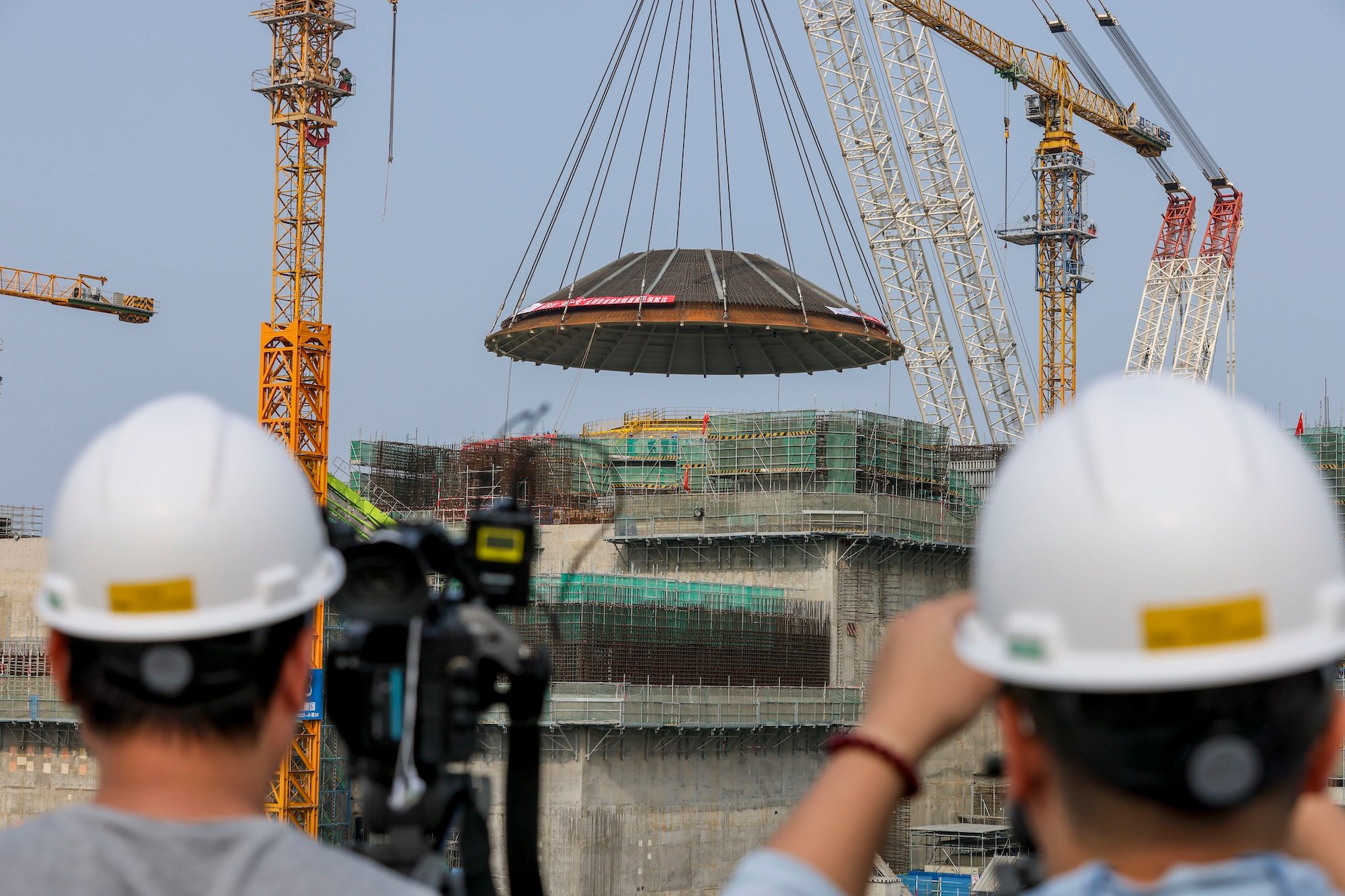 CHANGJIANG, CHINA - FEBRUARY 06: Reporters take photos of a 550-ton outer dome being hoisted in place at the construction site of the World's first commercial small modular reactor Linglong One, marking the main structure of its reactor building completed, on February 6, 2024 in Changjiang Li Autonomous County, Hainan Province of China. The reactor is expected to generate 1 bln kWh of power annually for 526,000 households upon operation. (Photo by Luo Yunfei/China News Service/VCG )No Use China.